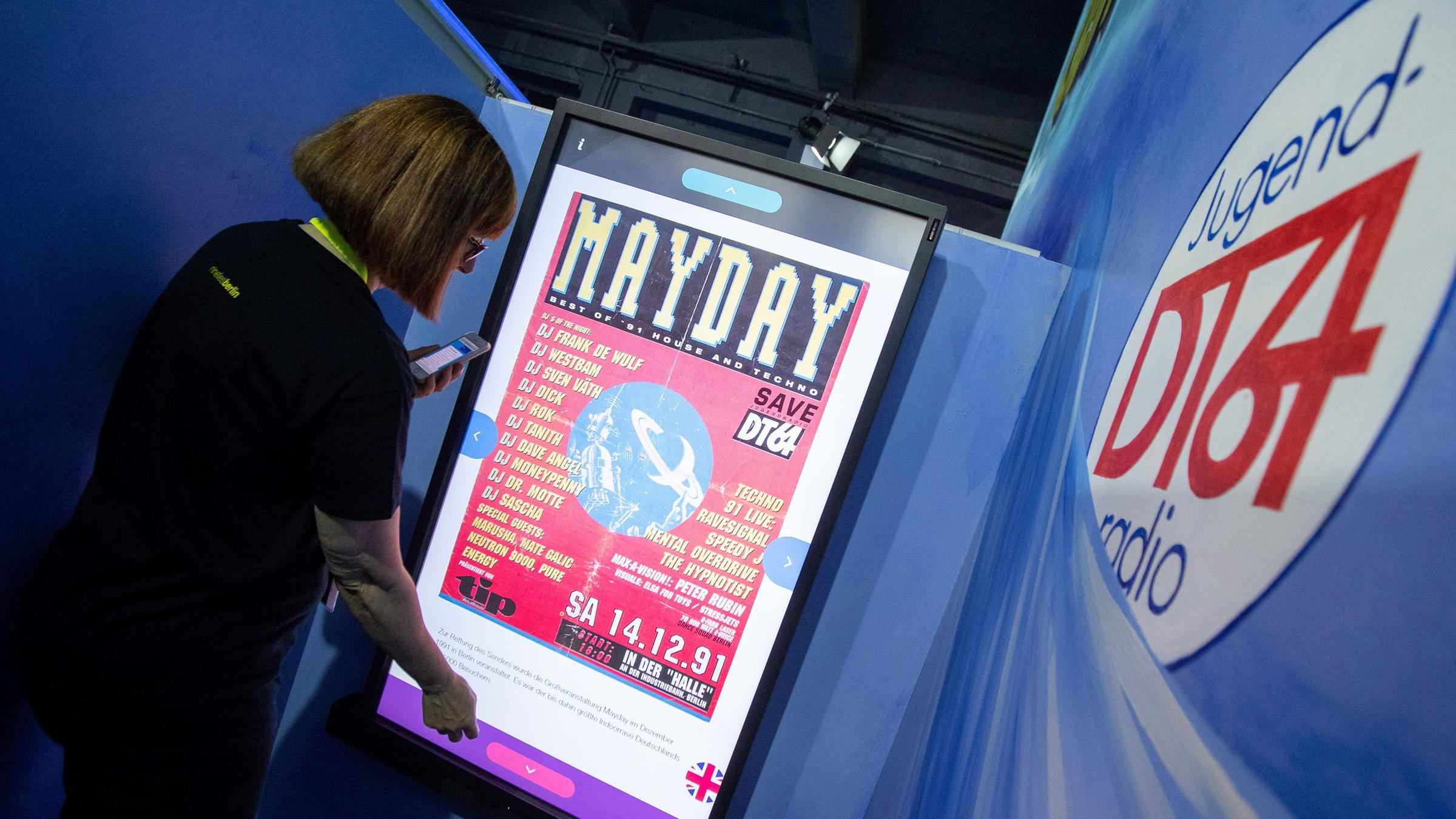 Eine Besucherin betrachtet ein altes Konzertposter auf einem Touchscreen