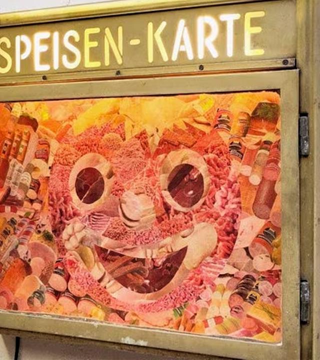 Man sieht einen Restaurant-Schaukasten der eine Collage in Form einer Gesichtswurst enthält.