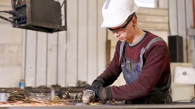Auszubildender Metallbauer beim Schleifen von Stahl in einer Fabrikhalle