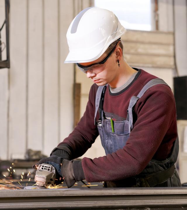 Auszubildender Metallbauer beim Schleifen von Stahl in einer Fabrikhalle
