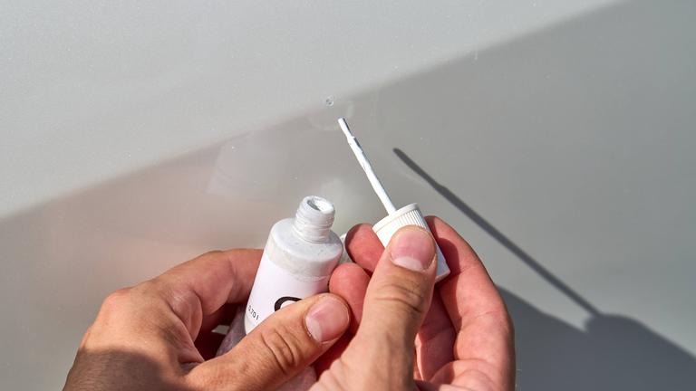 Eine Person bessert mit einem Lackstift einen Kratzer im Autolack aus.