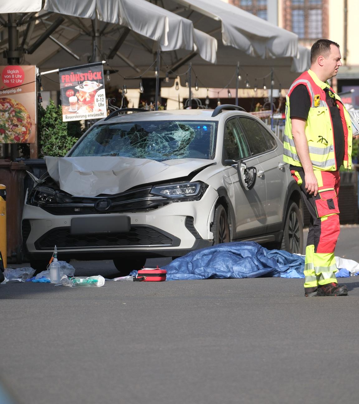 Sachsen, Leipzig: Rettungskräfte stehen neben einem beschädigten Auto.