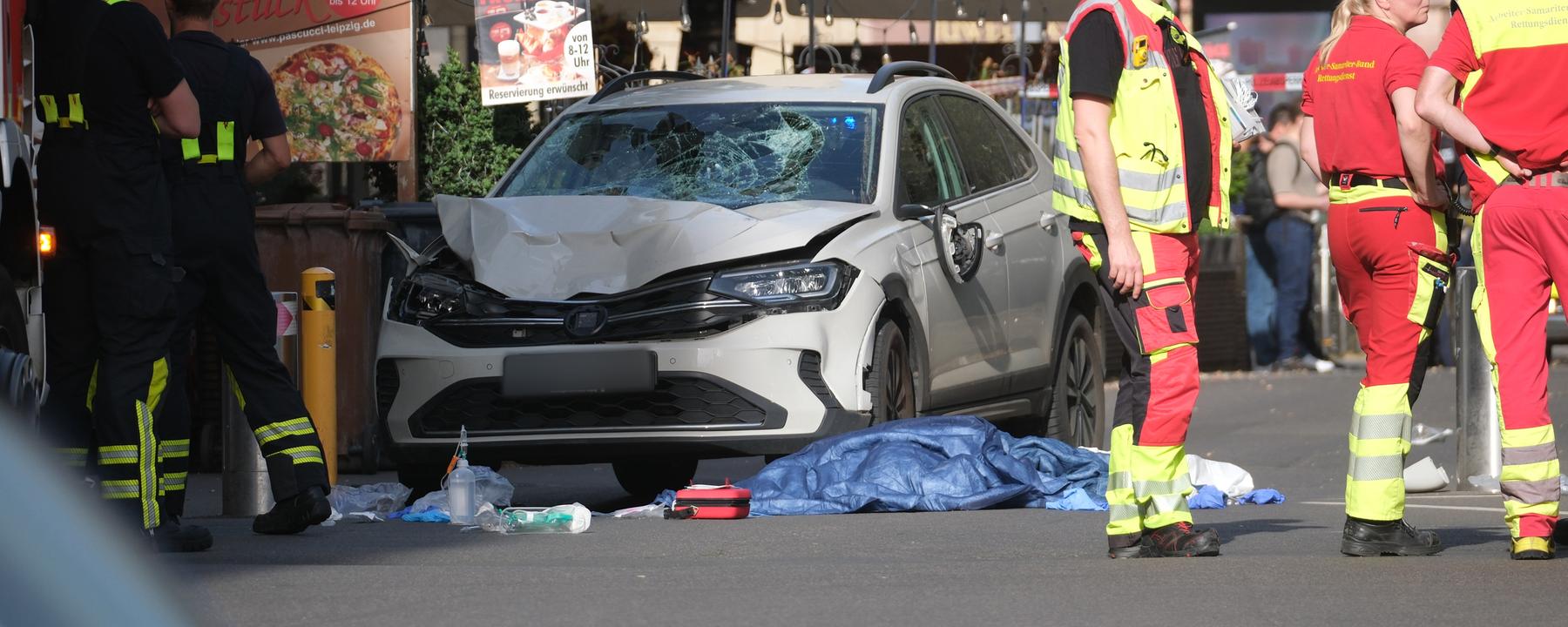 Sachsen, Leipzig: Rettungskräfte stehen neben einem beschädigten Auto.