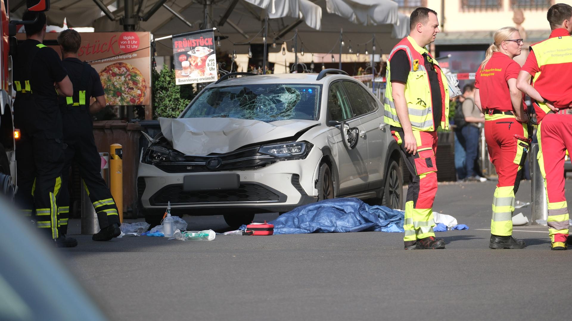 Sachsen, Leipzig: Rettungskräfte stehen neben einem beschädigten Auto.