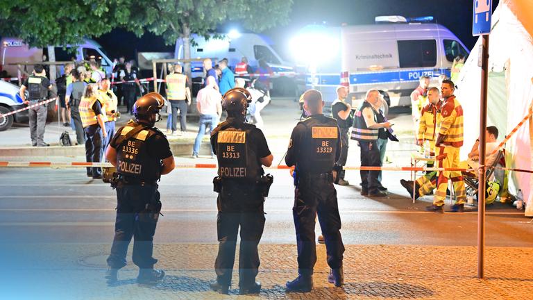 Drei Polizisten stehen am Einsatzort. Im Hintergrund stehen andere Rettungskräfte und Einsatzfahrzeuge
