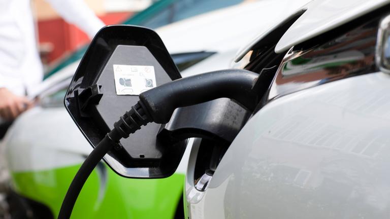 Nahaufnahme eines elektrischen Plug-in-Hybridautos am Bahnhof mit einem Mann im Hintergrund,