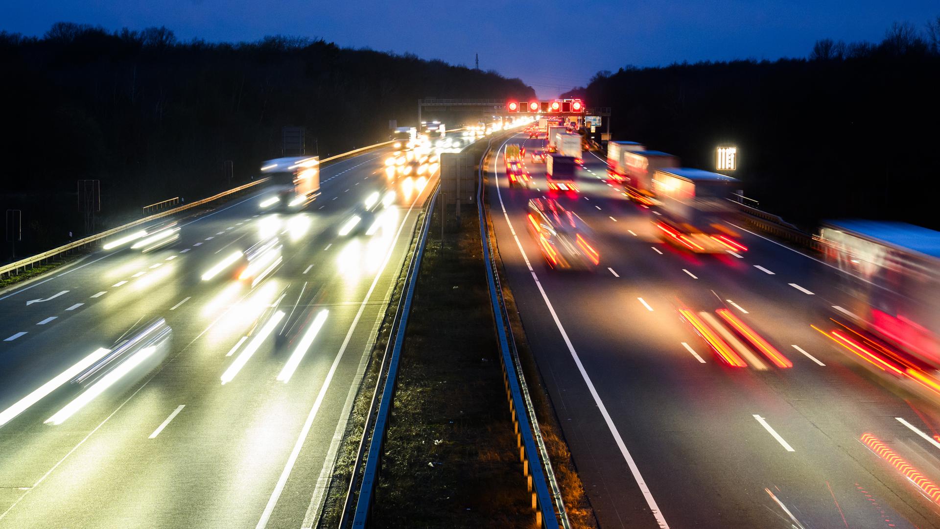 Eine stark befahrene Autobahn in der Dämmerung, die Scheinwerfer der Autos werfen ein verzerrtes orangenes, rotes und weißes Licht.