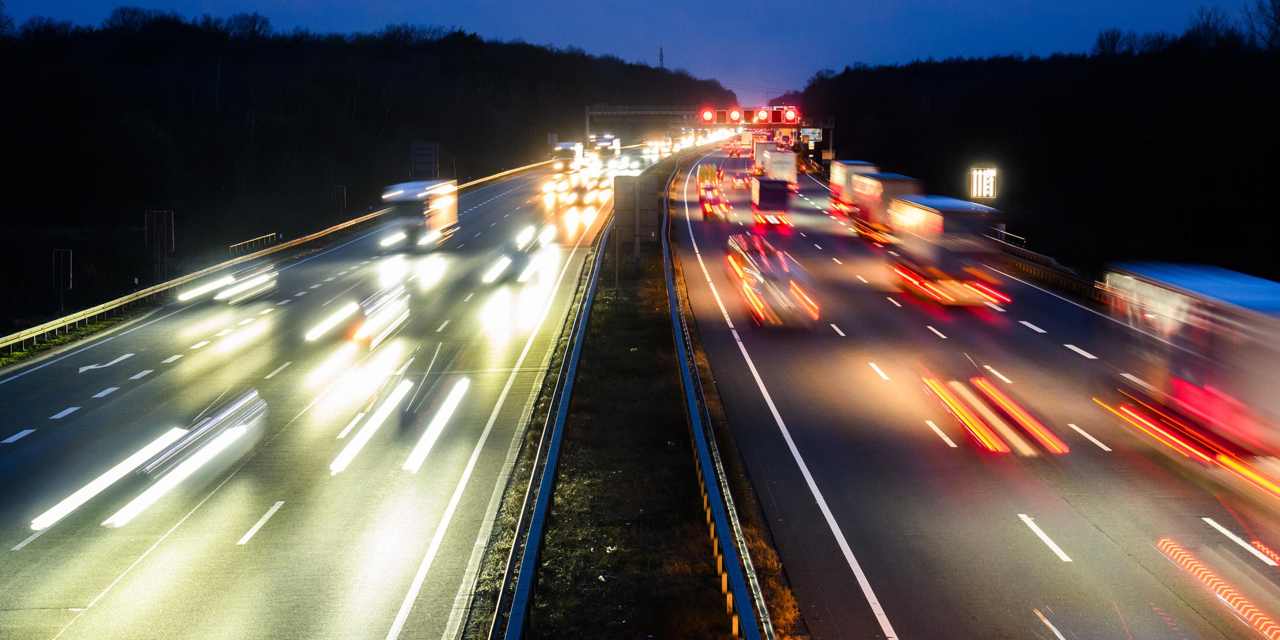 Eine stark befahrene Autobahn in der Dämmerung, die Scheinwerfer der Autos werfen ein verzerrtes orangenes, rotes und weißes Licht.