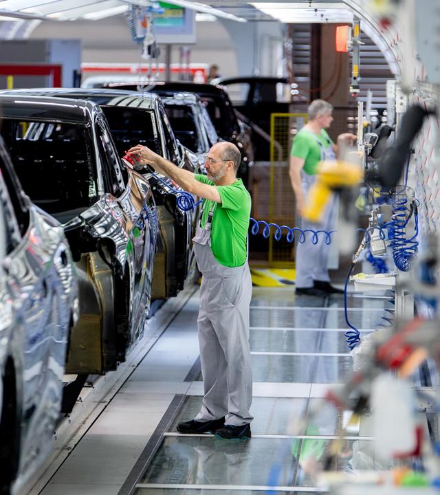 Mitarbeiter überprüfen im Lichttunnel der Lackiererei im Werk von Volkswagen den Lack einer Karosserie