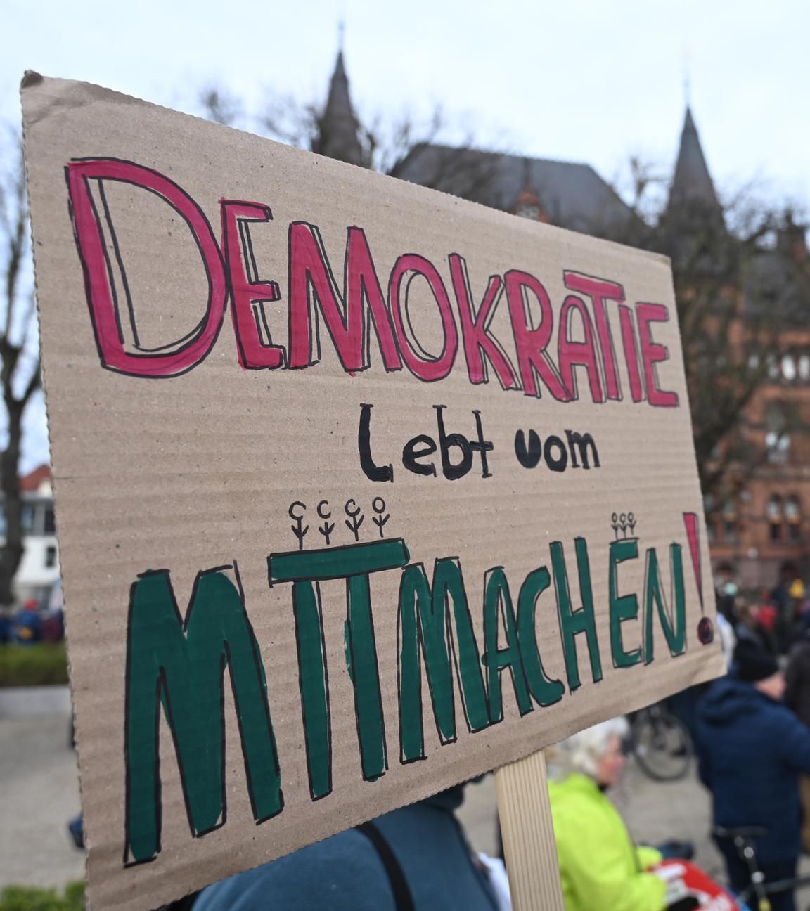 22.02.2025, Mecklenburg-Vorpommern, Rostock: Teilnehmer einer Demonstration und Kundgebung unter dem Motto "Solidarität statt Ausgrenzung" zeigen in der Innenstadt ein Plakat mit der Aufschrift "Demokratie lebt vom Mitmachen!".