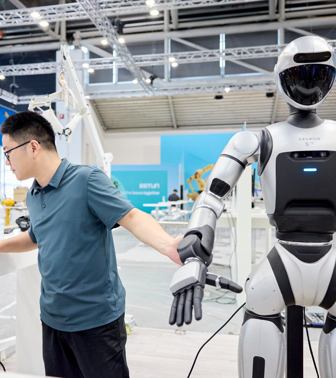 Mann steht neben Roboter und arbeitet am Laptop.