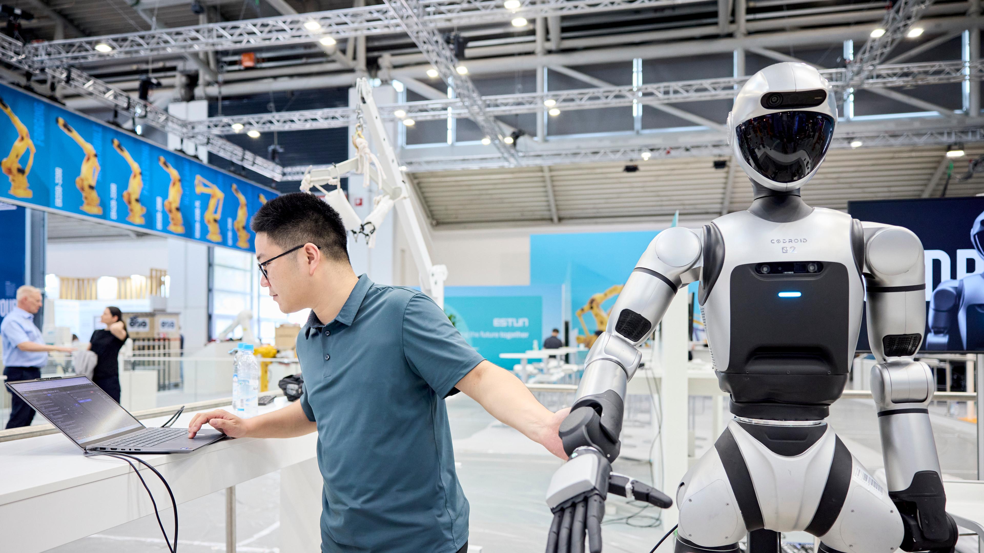 Mann steht neben Roboter und arbeitet am Laptop.
