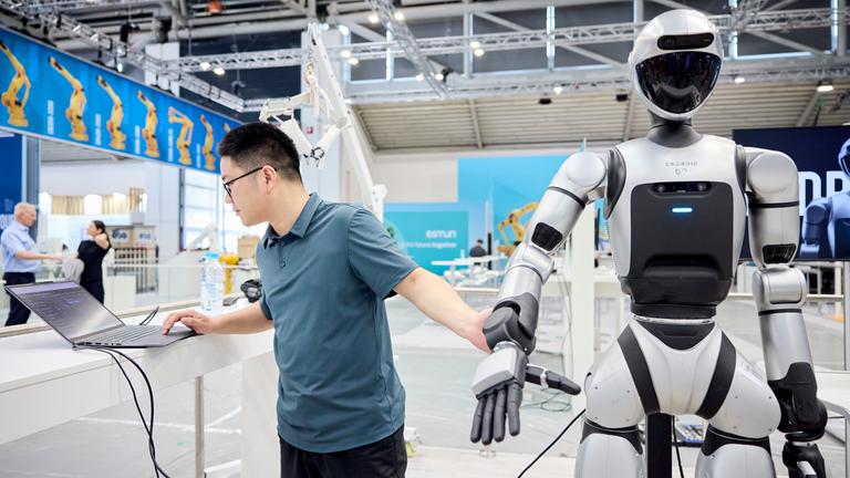 Mann steht neben Roboter und arbeitet am Laptop.