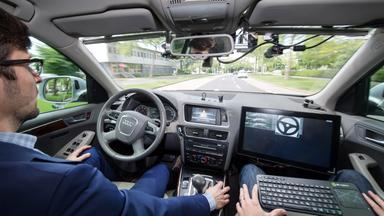 Ein selbstfahrendes Auto des Dorschungszentrums Informatik fährt mit zwei Entwicklern im Straßenverkehr.
