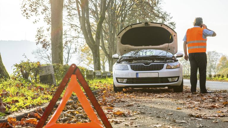 Symbolbild: Rückansicht eines Mannes, der mit seinem Handy telefoniert, nachdem sein Auto eine Panne hatte