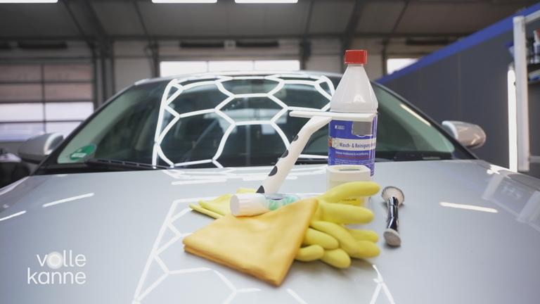 Auto auf dessen Motorhaube verschiedene Reinigungs-Gegenstände liegen