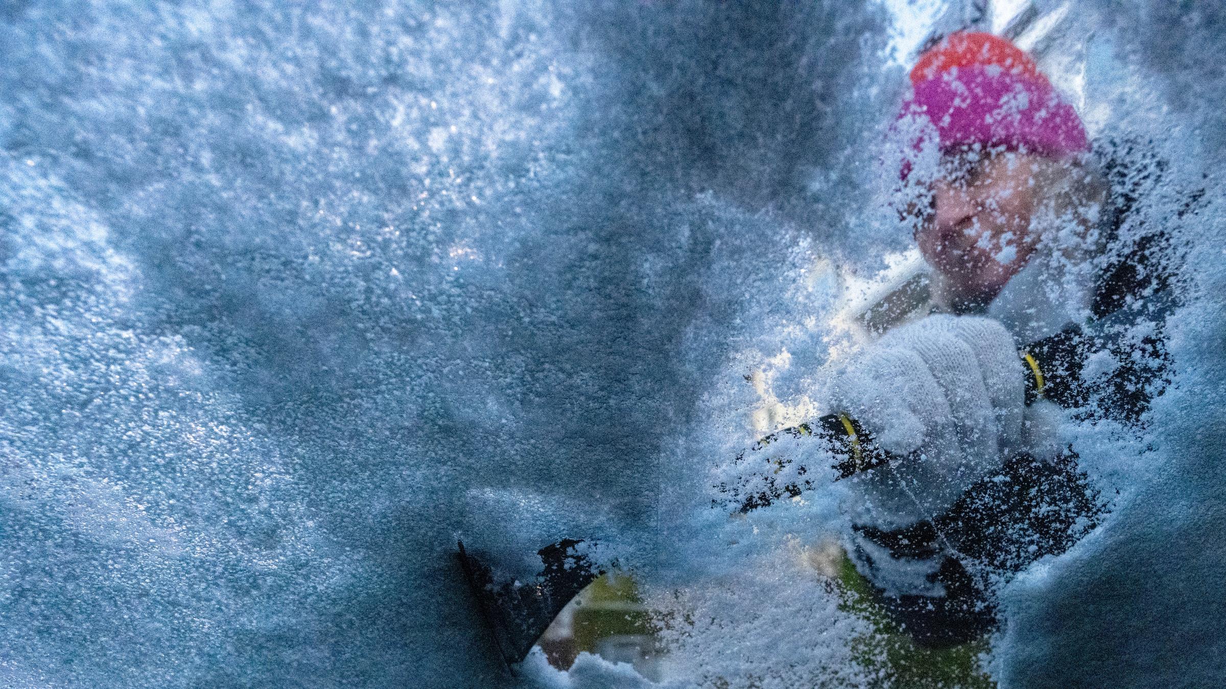 Eine Person befreit eine Autoscheibe mit einem Kratzer von Eis und Schnee.