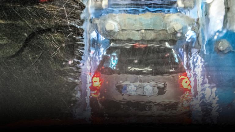 Autowaschanlage von Aral, Blick aus dem Wageninneren auf die rotierenden Bürsten und das vordere Fahrzeug auf dem Förderband,