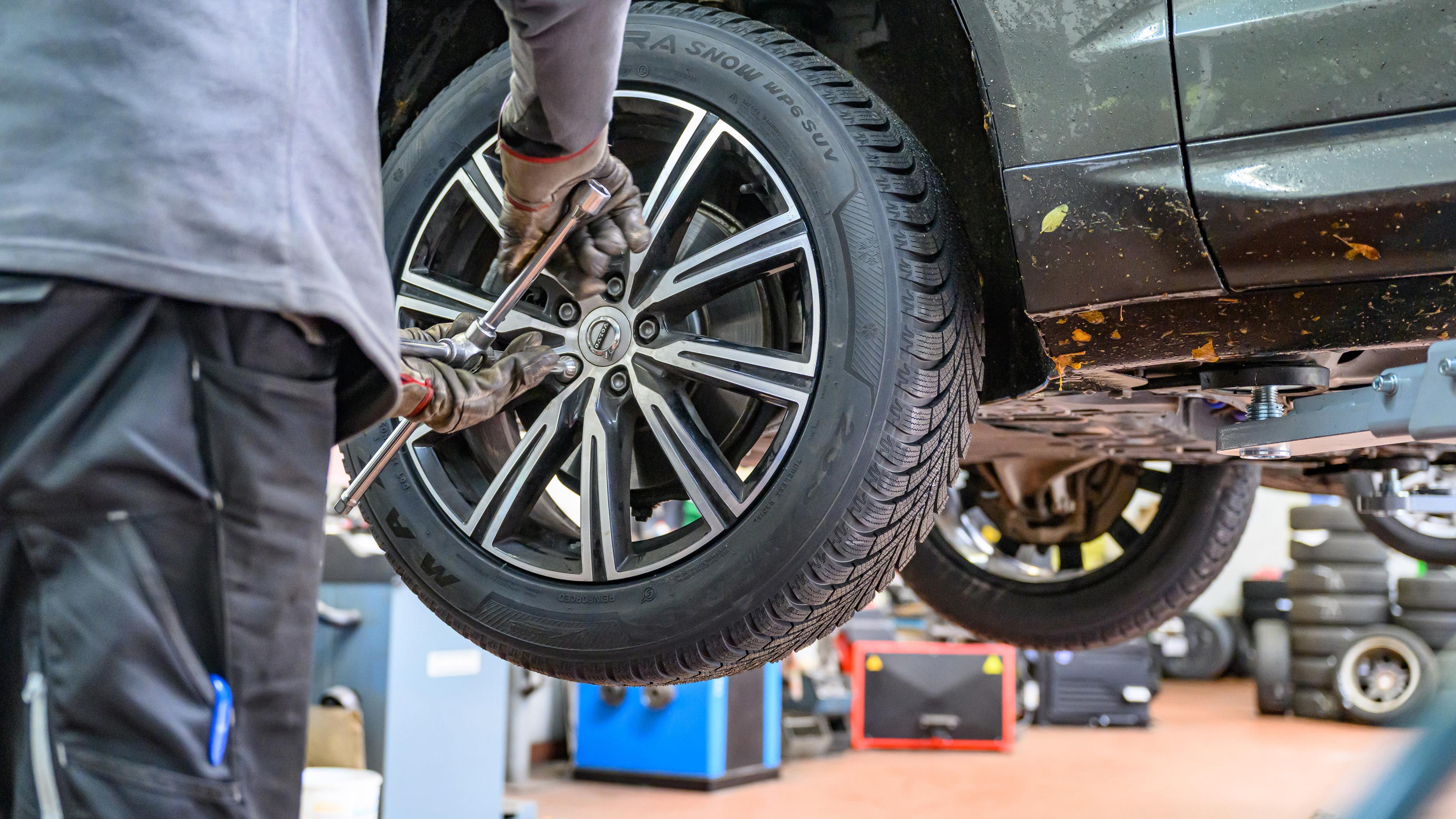 Ein Winterreifen wird in einer Werkstatt an ein Auto montiert