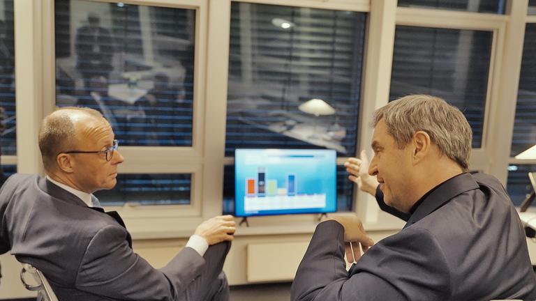 Friedrich Merz und Markus Söder sitzen vor einem Bildschirm mit Balkendiagramm.