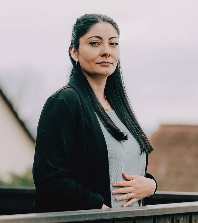 Aylin (rechts im Bild) steht auf einem Balkon. Sie schaut Ernst in die Kamera und hält fasst sich mit der Hand an den Bauch.
