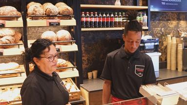 Zwei Personen die hinter einer Bäckereitheke stehen. 