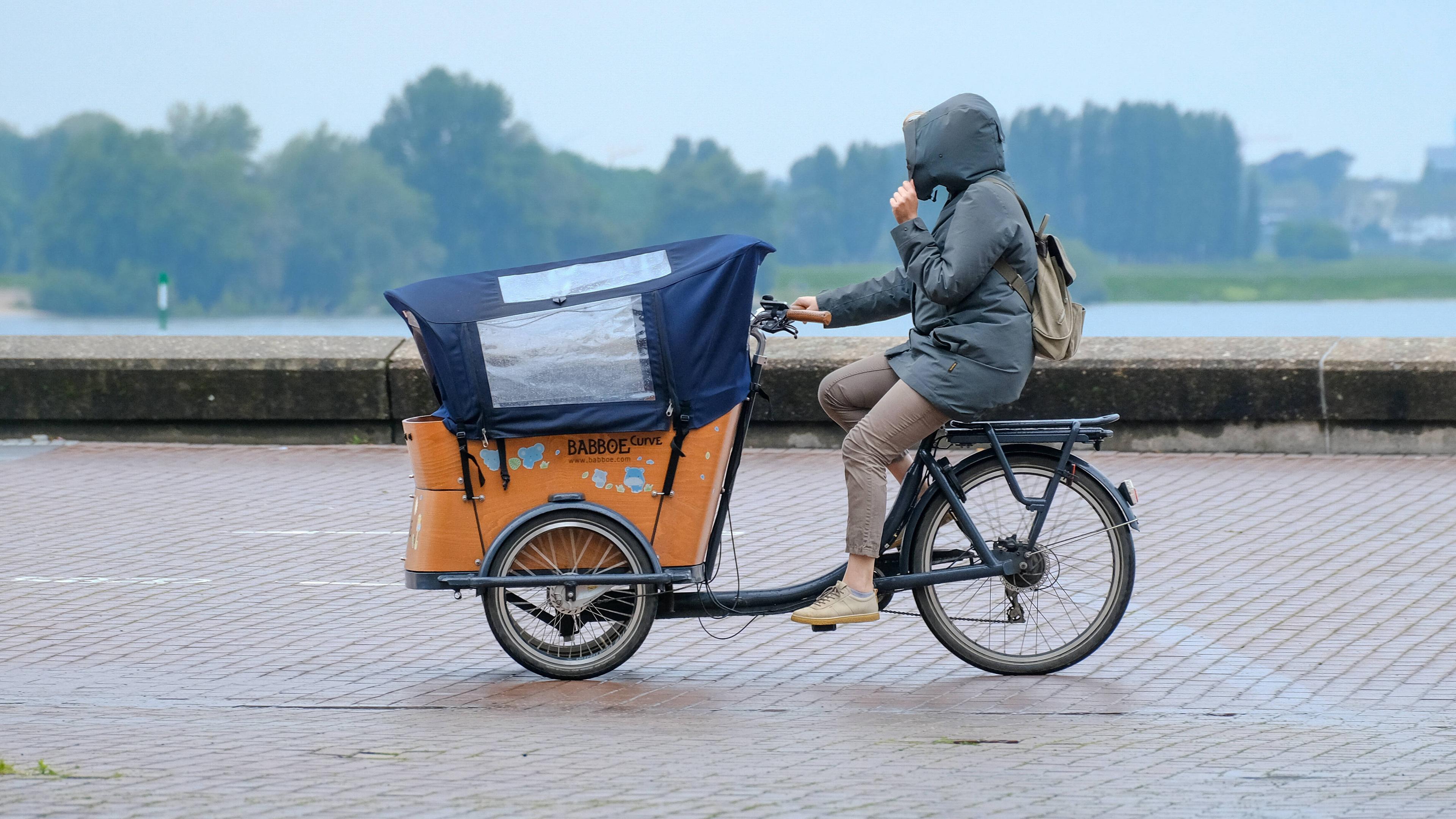 Frau fährt auf einem Lastenfahrrad durch den Regen