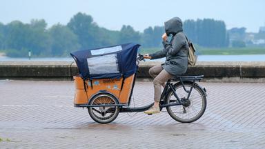 Frau fährt auf einem Lastenfahrrad durch den Regen