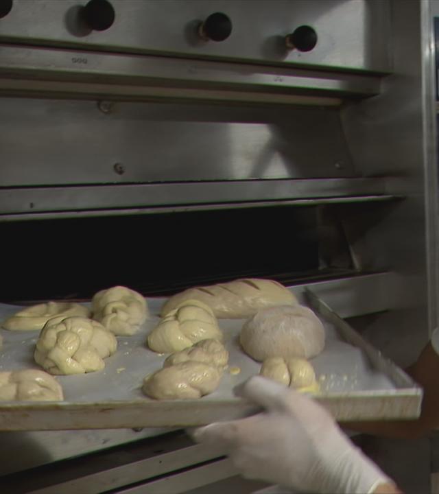 Ein Mitarbeiter schiebt ein Blech mit Brötchen in den Ofen.