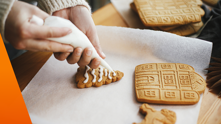 Weihnachtsgebäck auf Backpapier: ein Tannenbaum-Plätzchen wird mit weißer Glasur verziert 