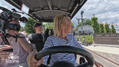 Andrea Kiewel fährt mit Golfcar über Gelände vom ZDF-Fernsehgarten.