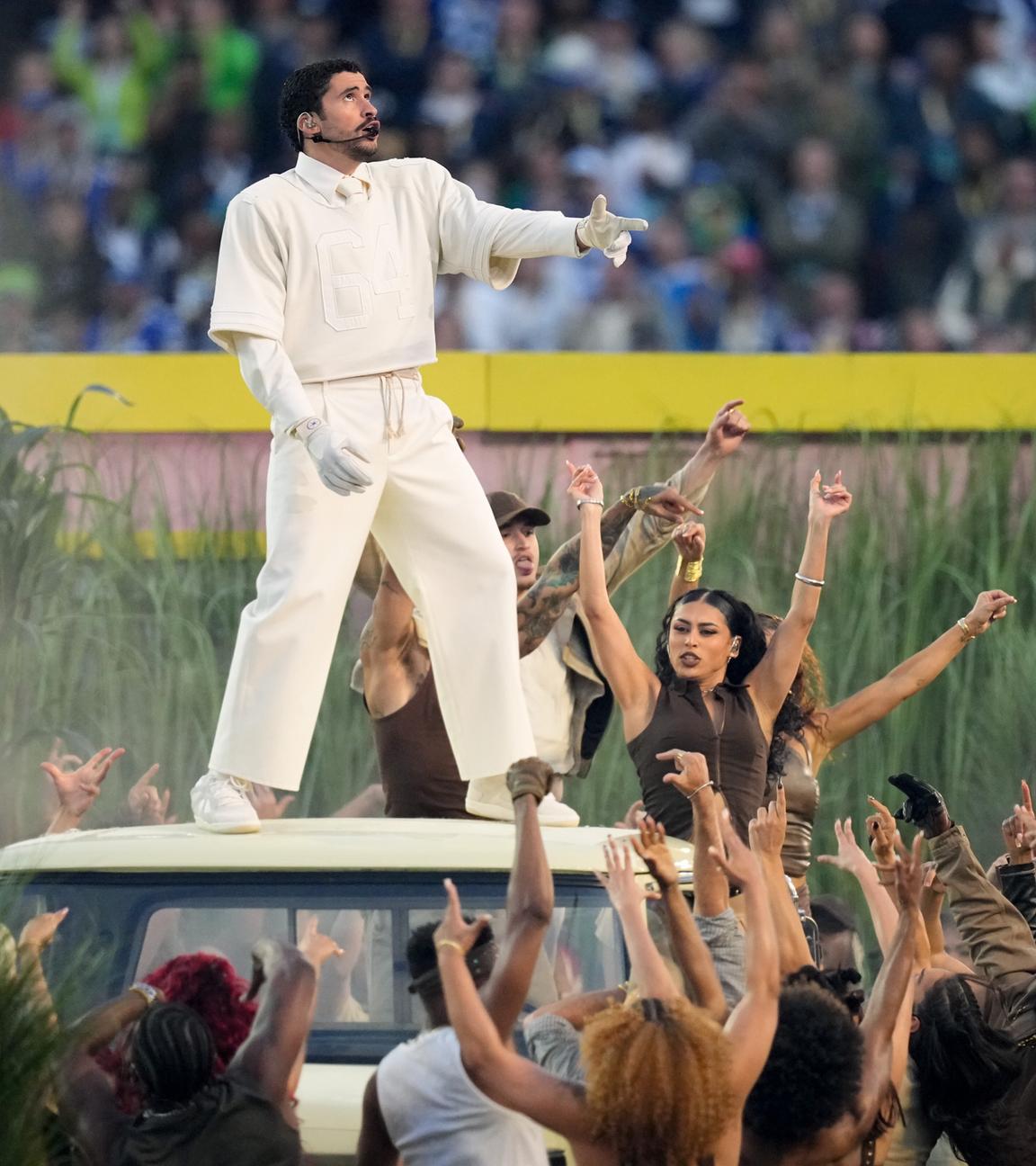 Bad Bunny bei seiner Halbzeitshow im weißen Anzug, steht auf dem Dach eines Autos und singt.