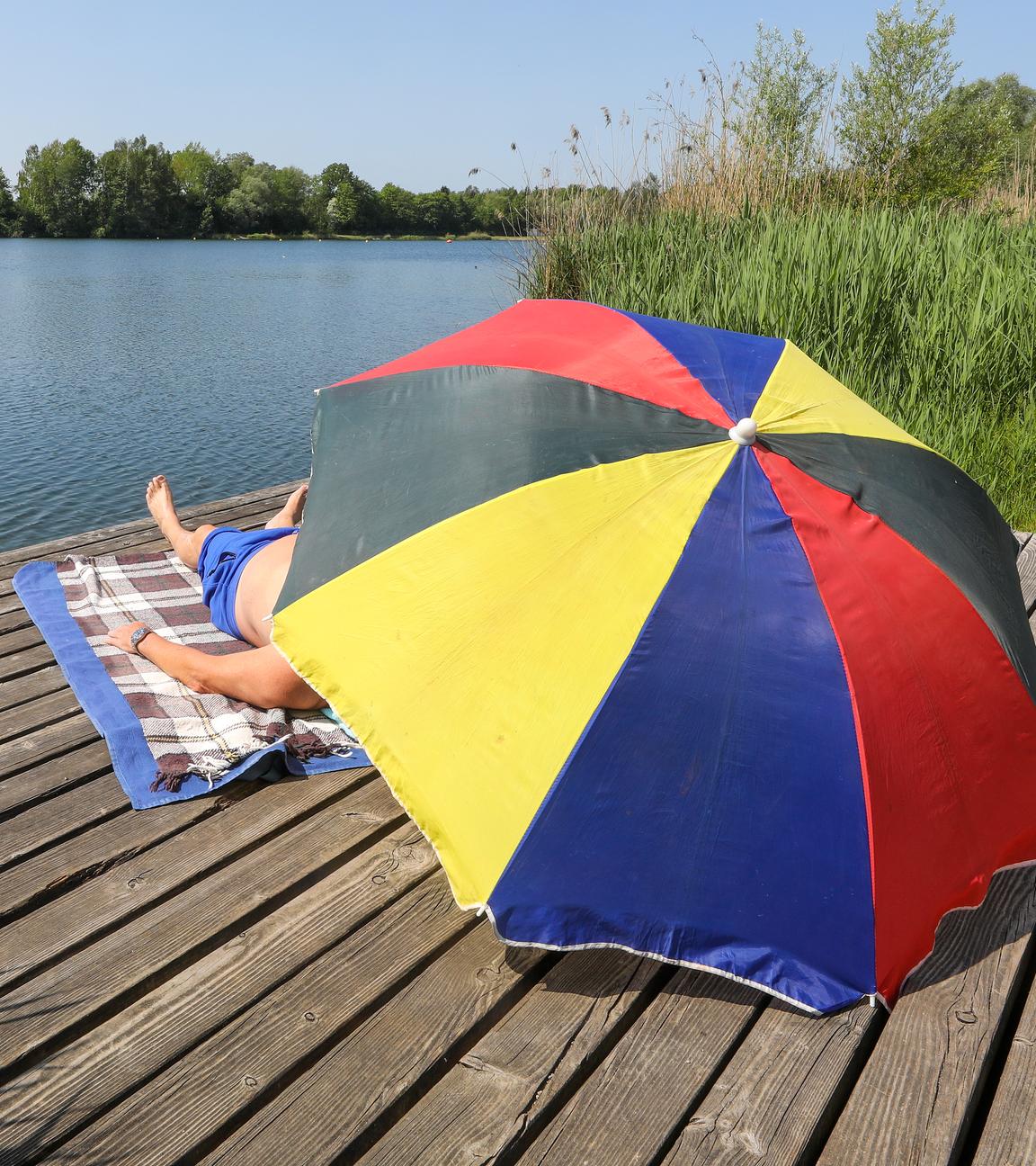 Menschen unter Sonnenschirm an einem Badesee.