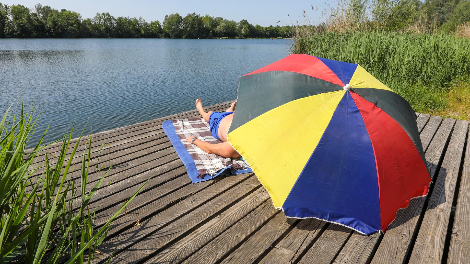 Menschen unter Sonnenschirm an einem Badesee.
