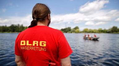 Ein Vertreter der DLRG blickt auf einen Badesee, auf dem sich ein Boot zur Lebensrettung befindet.