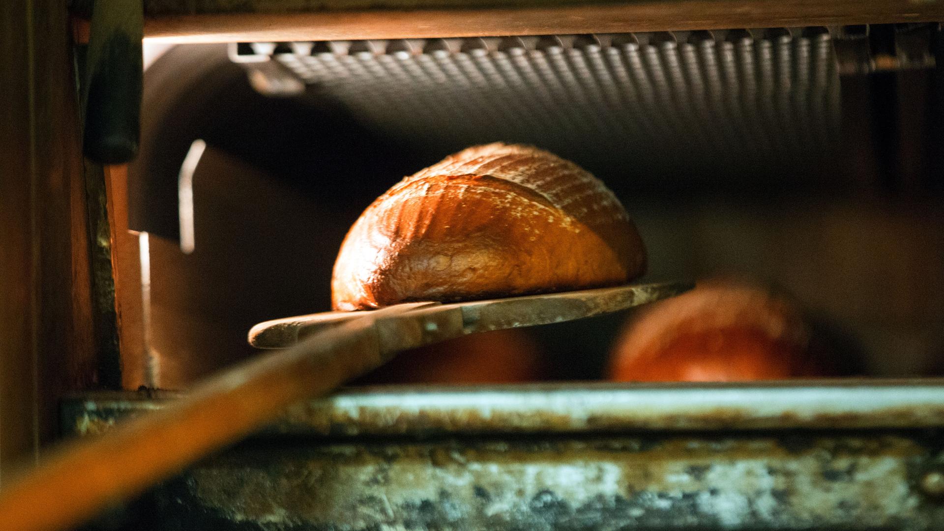 Ein Brot wird mit einem Brotschieber aus dem heißen Ofen geholt.