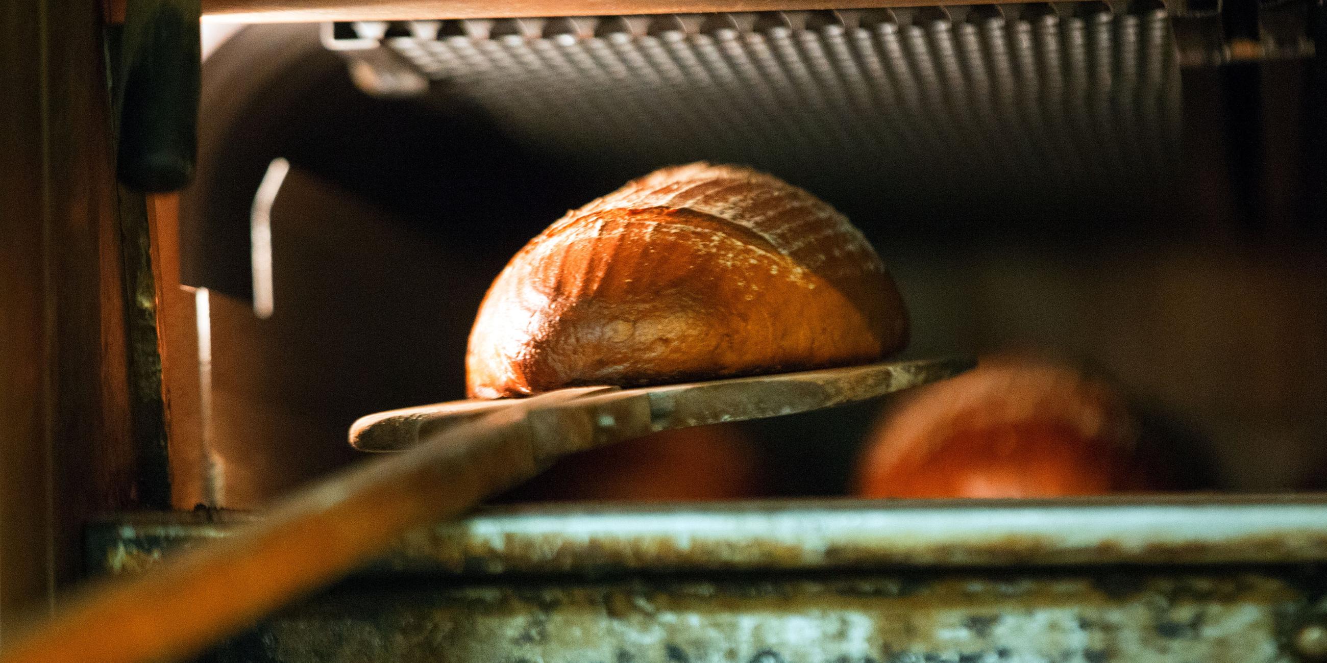 Ein Brot wird mit einem Brotschieber aus dem heißen Ofen geholt.