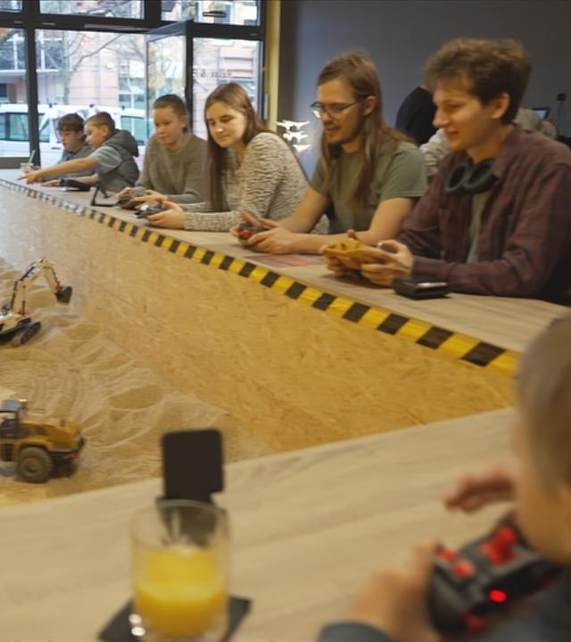 Menschen, die um Sandgrube sitzen und Kaffee trinken, während sie Baufahrzeuge steuern