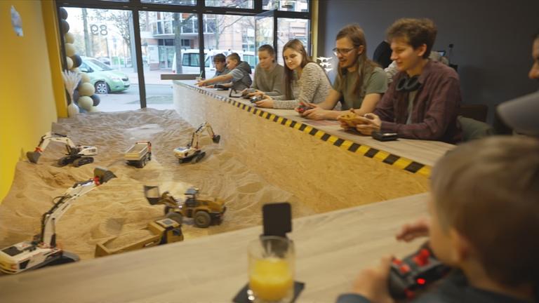 Menschen, die um Sandgrube sitzen und Kaffee trinken, während sie Baufahrzeuge steuern