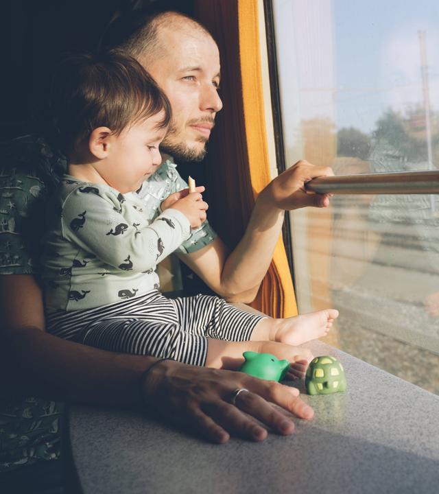 Vater und Kind sitzen in einer Bahn und schauen aus dem Fenster.