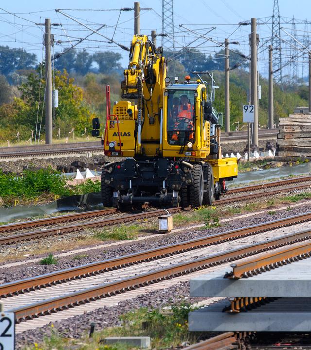  Gleisbaufahrzeuge rollen nahe des Bahnhofs Schönhausen an Gleisbauteilen vorbei. 