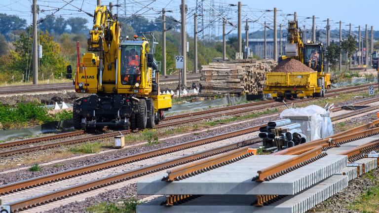  Gleisbaufahrzeuge rollen nahe des Bahnhofs Schönhausen an Gleisbauteilen vorbei. 