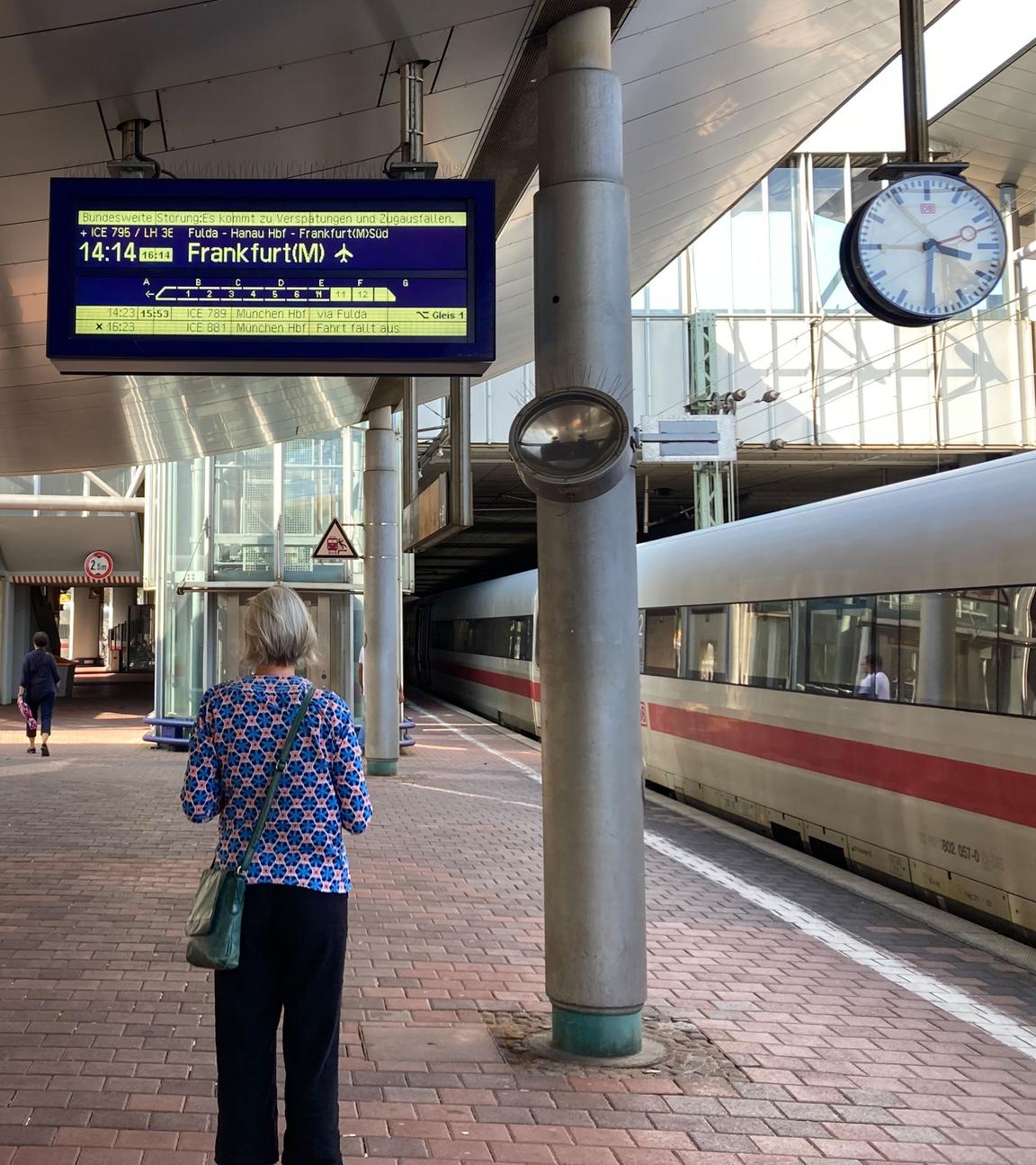 Eine Frau steht auf dem Bahnsteig und schaut sich eine Anzeige der Deutsche Bahn an.