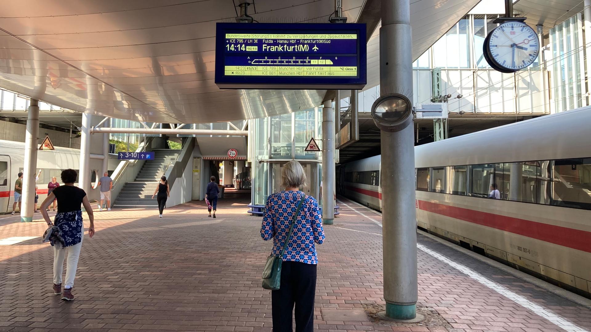 Eine Frau steht auf dem Bahnsteig und schaut sich eine Anzeige der Deutsche Bahn an.