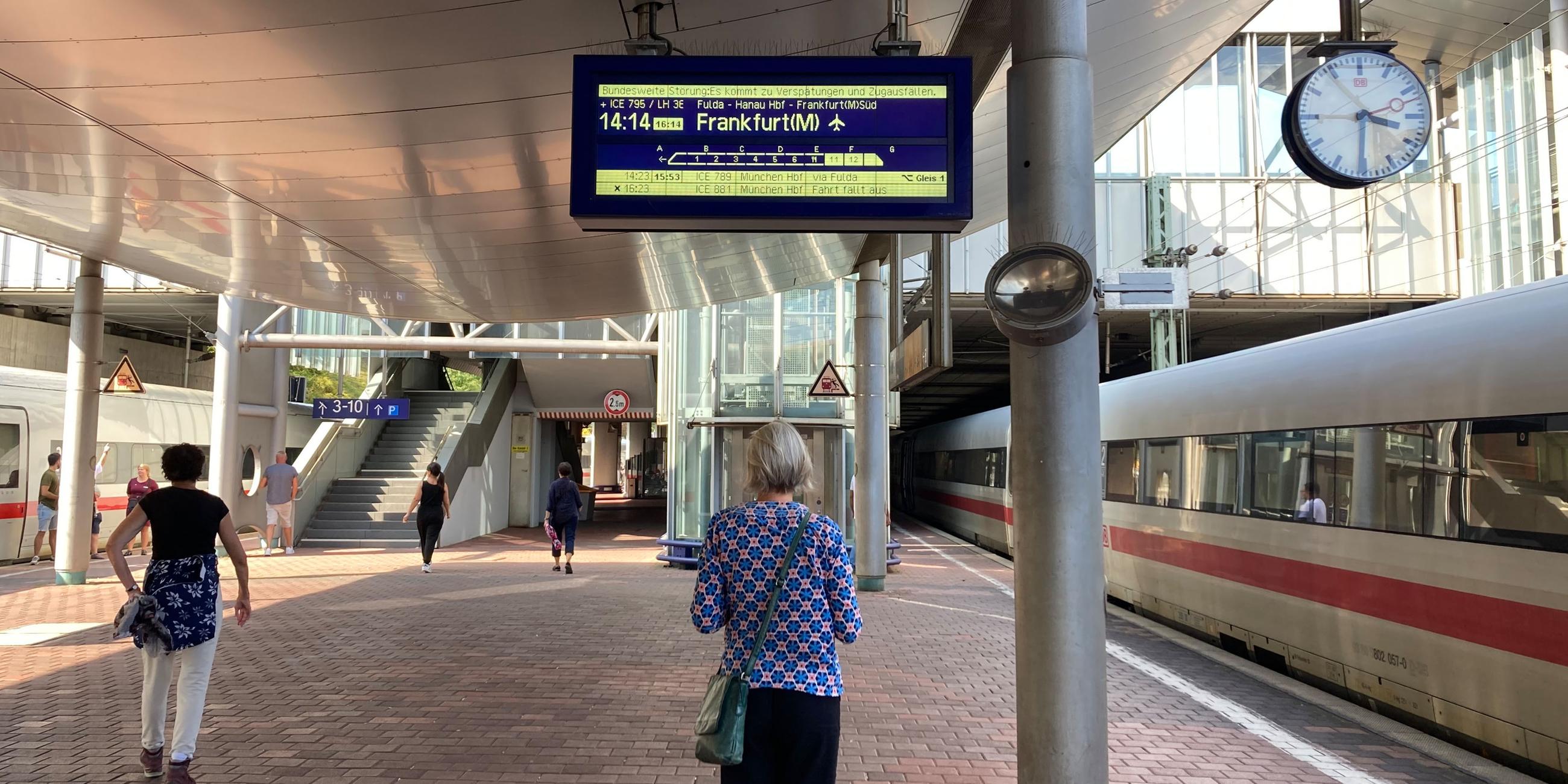 Eine Frau steht auf dem Bahnsteig und schaut sich eine Anzeige der Deutsche Bahn an.