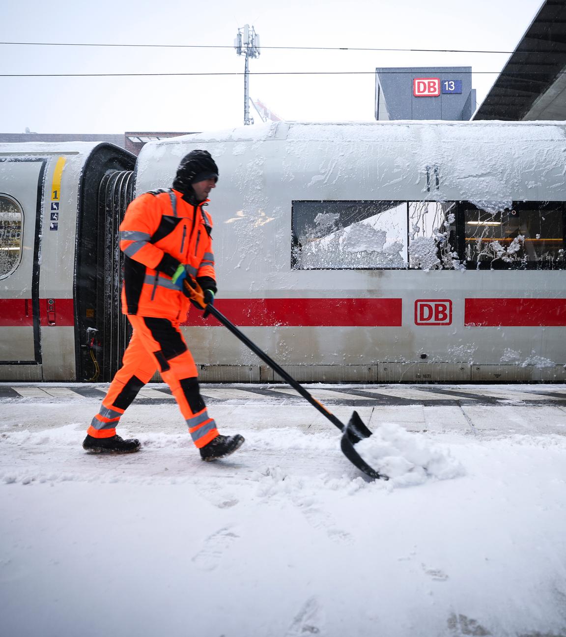 Ein Mitarbeiter schiebt Schnee von einem Bahnsteig am Hauptbahnhof an dem ein abgestellter ICE steht. 