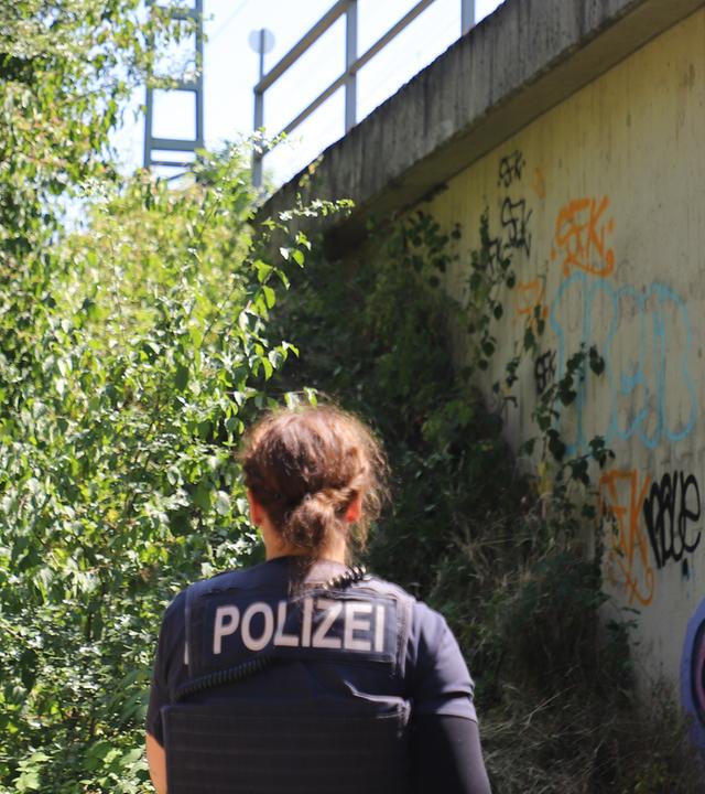 Eine Polizistin steht unter einer Brücke an einer Bahnstrecke.