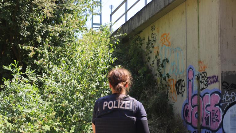 Eine Polizistin steht unter einer Brücke an einer Bahnstrecke.