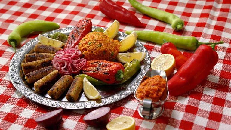 Eine silberne Platte mit vegetarischen Cevapcici, Balkanreis und diversen Gemüsesorten