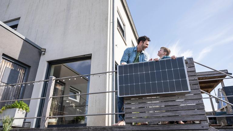 Balkonkraftwerk am Geländer von einem Balkon an einer Wohnung, Vater und Sohn dahinter.